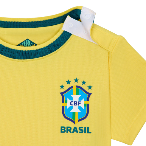 A close-up shot of a bright yellow baby-sized Brazil national football team jersey. It features a dark green ribbed neckline and a white snap-button opening on the shoulder. The official CBF crest is printed on the front with five green stars above it and