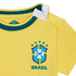 A close-up shot of a bright yellow baby-sized Brazil national football team jersey. It features a dark green ribbed neckline and a white snap-button opening on the shoulder. The official CBF crest is printed on the front with five green stars above it and