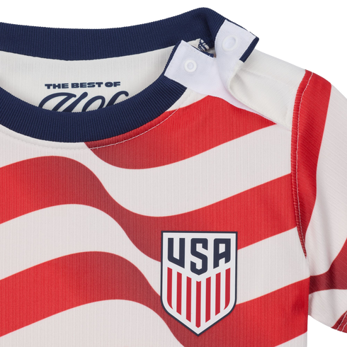 Close-up of a baby shirt with red and white wavy stripes, a navy blue collar, shoulder snaps, and the USA soccer team crest on the chest.