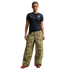 A woman stands against a black background wearing a navy USA soccer jersey, oversized camouflage cargo pants, and red sneakers.