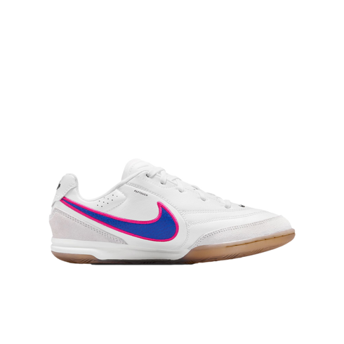 A white Nike indoor soccer shoe with a blue and pink swoosh and gum rubber outsole, shown in profile against a black background.