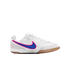 A white Nike indoor soccer shoe with a blue and pink swoosh and gum rubber outsole, shown in profile against a black background.