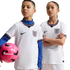 Two children pose in white England national team football kits against a black background. The boy holds a pink football.