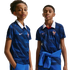 Two youths wear blue France national team jerseys with white collars and diagonal stripes. The shirts feature the FFF rooster crest. Solid black background.