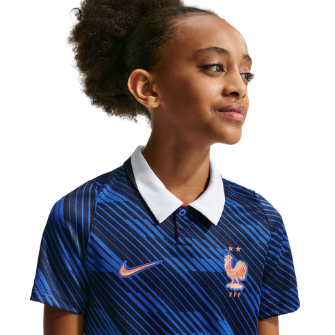 A young girl in a blue patterned France national team soccer jersey with a white collar, looking off-camera against a black background.