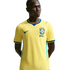 A young Black man wearing a yellow Nike Brazil national football team home jersey with blue trim, standing against a solid black background.