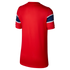 Back view of a red short-sleeved jersey displayed against a solid black background. The shirt features a subtle vertical-striped texture in the fabric. Each sleeve is detailed with a wide horizontal blue band that contains a tonal pattern, bordered by thi