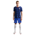 A man in a blue patterned France national football kit with a white collar, blue shorts, and white socks, standing against a black background.