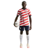A male soccer player in a wavy red and white USA jersey and navy shorts, holding a soccer ball under his arm against a black background.