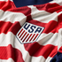 Close-up of a textured red and white striped USA soccer jersey with the official team shield crest in the center.
