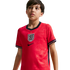 A young boy wearing a red England national football team jersey with the Three Lions crest, looking off-camera against a black background.
