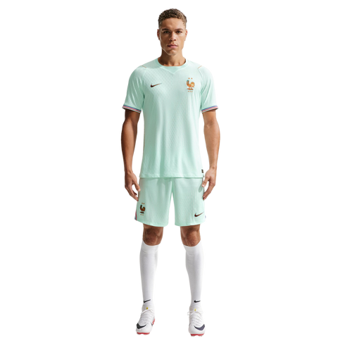 A man models a light mint green Nike France soccer kit with white socks and cleats against a black background.