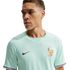 A man wears a mint green France national soccer team jersey with a golden rooster crest and tricolor sleeve cuffs, looking away against a black background.