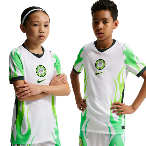 Two children, one with arms crossed and one with hands on hips, wear Nigeria national soccer jerseys featuring white and green flame designs against a black background.