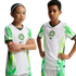 Two children, one with arms crossed and one with hands on hips, wear Nigeria national soccer jerseys featuring white and green flame designs against a black background.