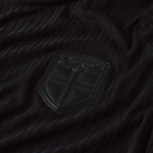 Close-up of a black textured jersey featuring a matte black shield crest with the word "NORGE" and a Nordic cross motif.