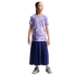 A young girl in a purple floral Nike South Korea soccer jersey, long navy pleated skirt, and gray sneakers, standing against a black background.