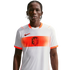 A young man with braided hair wears a white Netherlands national football team away jersey with a horizontal orange patterned band, the KNVB lion crest, and a black Nike swoosh, set against a solid black background.