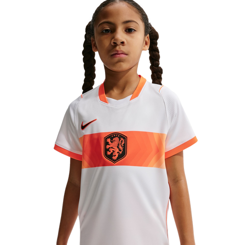 A young girl with braided hair wearing a white and orange Netherlands national team soccer jersey against a black background.