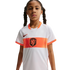 A young girl with braided hair wearing a white and orange Netherlands national team soccer jersey against a black background.
