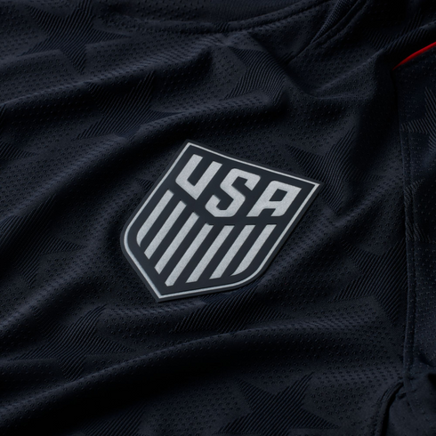 Close-up of a black US Soccer jersey featuring a silver crest and a subtle, tonal star pattern in the textured fabric.
