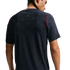 Back view of a man with braided hair wearing a dark navy t-shirt featuring a subtle star pattern and red piping on the shoulders, set against a plain black background.