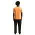 Back view of a person with dark curly hair wearing an orange shirt with green trim and black pants against a black background.
