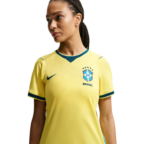 A woman with braided hair wearing a yellow Brazil soccer jersey, looking away against a black background.