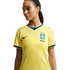 A woman with braided hair wearing a yellow Brazil soccer jersey, looking away against a black background.