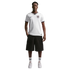 A man stands against a black background wearing a white England soccer jersey, black shorts, and white sneakers.