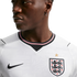 Close-up of a man in a white England national football team jersey with the Three Lions crest and Nike logo against a black background.