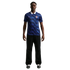 A man modeling a blue patterned France soccer jersey with a white collar, black trousers, and athletic shoes against a black background.