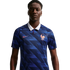 A man wearing a blue Nike France football jersey with a white collar and diagonal patterns, featuring a gold rooster crest and two stars, set against a black background.