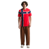 A young man stands against a black background wearing a red Nike Norway national team soccer jersey, brown baggy trousers, and white sneakers.