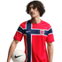 Man with curly hair wearing a red Norway national team soccer jersey and holding a white soccer ball against a black background.