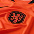 A close-up of a bright orange textured soccer jersey featuring the black KNVB shield crest with an orange lion rampant.