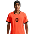 A man wearing a bright orange Netherlands national football team jersey and a black Nike beanie, centered against a solid black background. He has a mustache and visible tattoos on his arms.