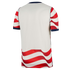 Back view of a white sports jersey with navy blue trim and red and white wavy stripes on the sleeves and bottom hem.