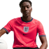 A man wearing a red England national football team jersey with the Three Lions crest and Nike logo, holding a white football against a black background.