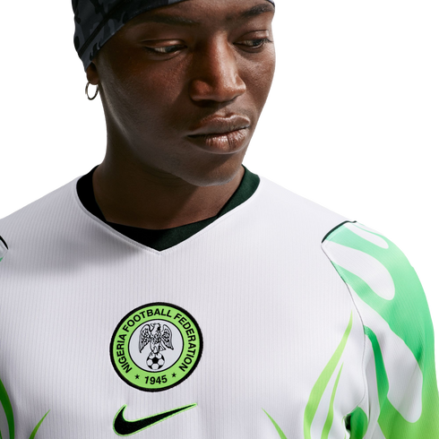 Close-up of a man wearing a white Nigeria national football team jersey with green leaf-patterned sleeves and the federation crest on the chest.