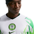 Close-up of a man wearing a white Nigeria national football team jersey with green leaf-patterned sleeves and the federation crest on the chest.