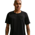 A man with a buzz cut and forearm tattoos wears a black Nike athletic shirt with a subtle monochromatic shield crest, standing against a dark background.