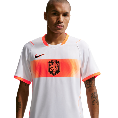 A waist-up portrait of a man wearing a white Netherlands national football team away jersey. The jersey features a wide orange band across the chest with a central lion crest and a black Nike logo on the right. The man has short-cropped hair, a mustache,