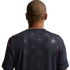 Back view of a man with a buzz cut wearing a navy blue jersey with a tonal star pattern and red shoulder piping, set against a black background.