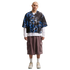A man wears an oversized blue and black patterned Nike jersey, white long-sleeve shirt, baggy brown cargo shorts, and cream sneakers against a white background.