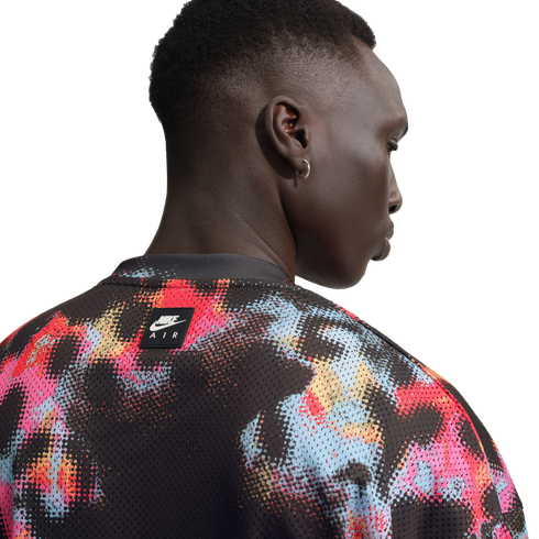A close-up, back-profile view of a person wearing a black mesh Nike Air shirt with a vibrant red, blue, and pink abstract paint-splatter pattern.