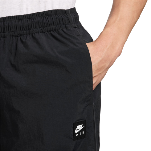 A close-up side view of a person wearing black Nike Air shorts with an elastic waistband, their hand tucked into a side pocket. A white Nike Air logo patch is visible on the thigh.