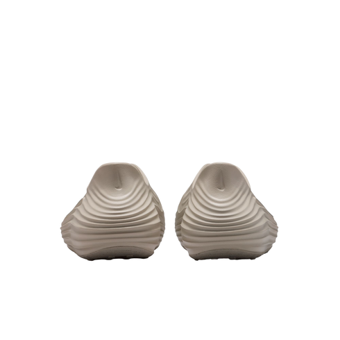 Rear view of two beige slip-on shoes with a unique rippled, wavy texture on the heels and small Nike swoosh logos, presented against a solid black background.