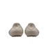 Rear view of two beige slip-on shoes with a unique rippled, wavy texture on the heels and small Nike swoosh logos, presented against a solid black background.