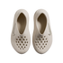 Top-down view of a pair of beige Nike foam clogs with perforated toes and textured sides, set against a black background.